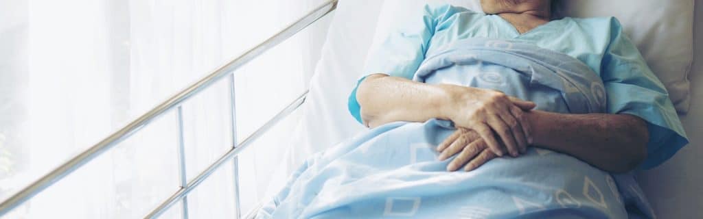 older woman laying in hospital bed with hands folded