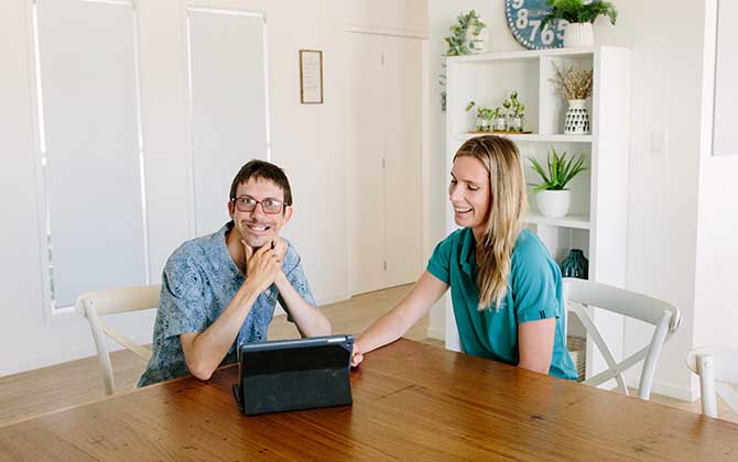 Client and clinician sitting at table using ipad for a therapy session where client is smiling at camera