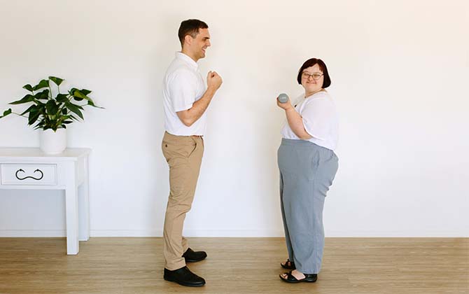 Physiotherapist helping client with therapy exercise where client is holding hand weight smiling at camera